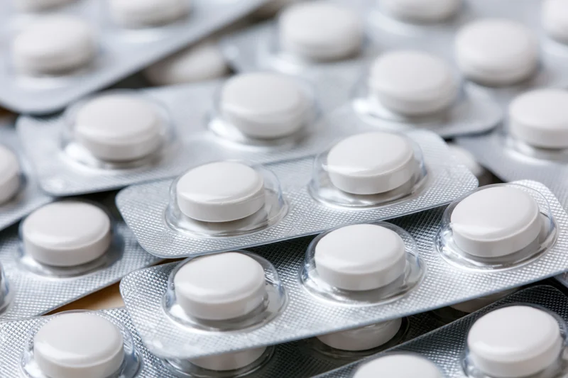 Multiple white round pills in blister packs stacked and layered on a reflective surface