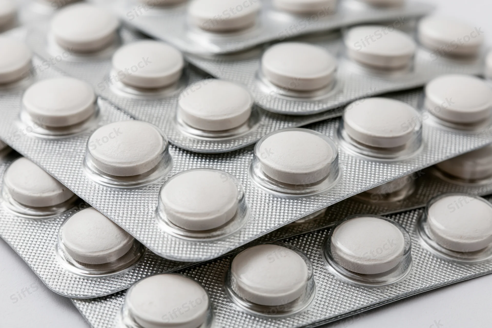 Stacked white round tablets in silver blister packs arranged in layers on a plain surface