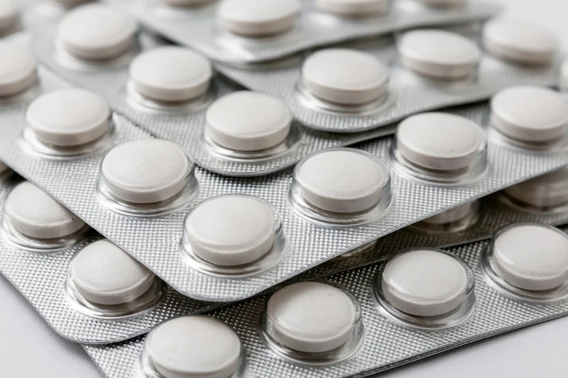 Stacked white round tablets in silver blister packs arranged in layers on a plain surface