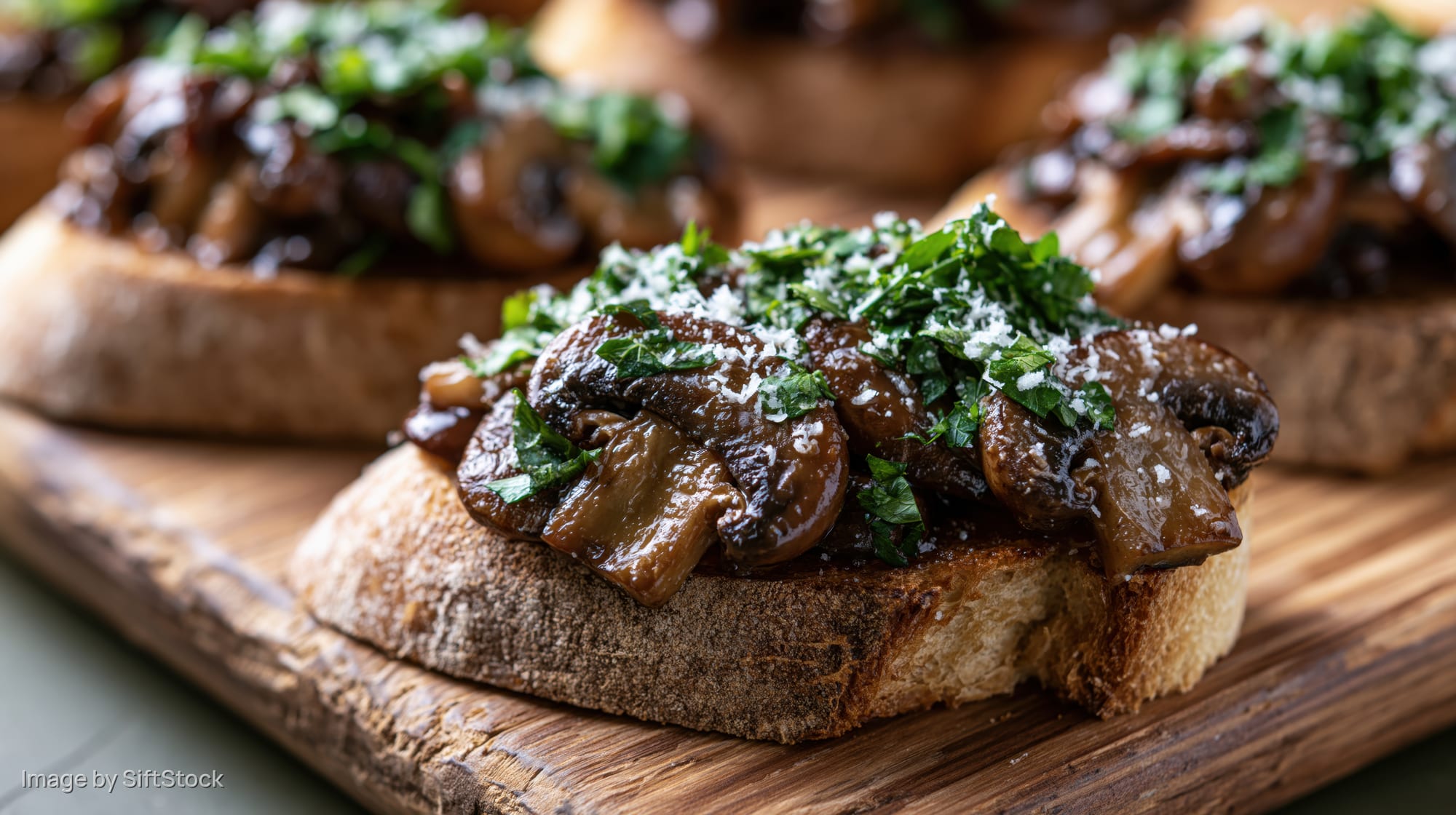 Mushroom bruschetta on toasted sourdough bread topped with parsley and cheese on a wooden cutting board
