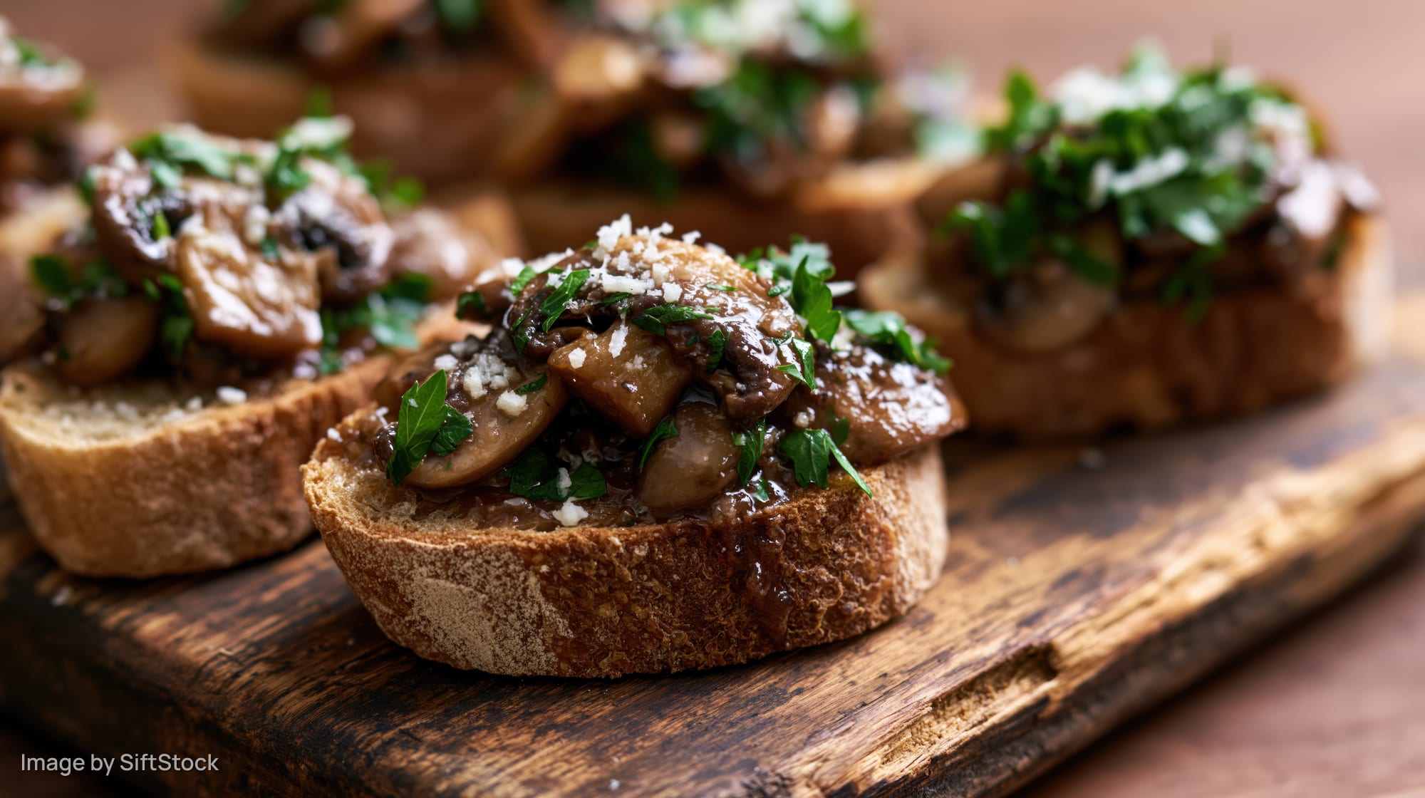 Mushroom bruschetta on toasted sourdough bread topped with parsley and cheese on a wooden board