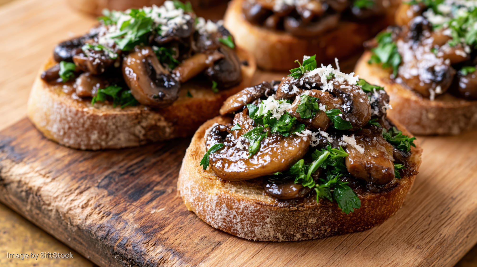Mushroom bruschetta on toasted sourdough bread topped with parsley and parmesan on a wooden cutting board