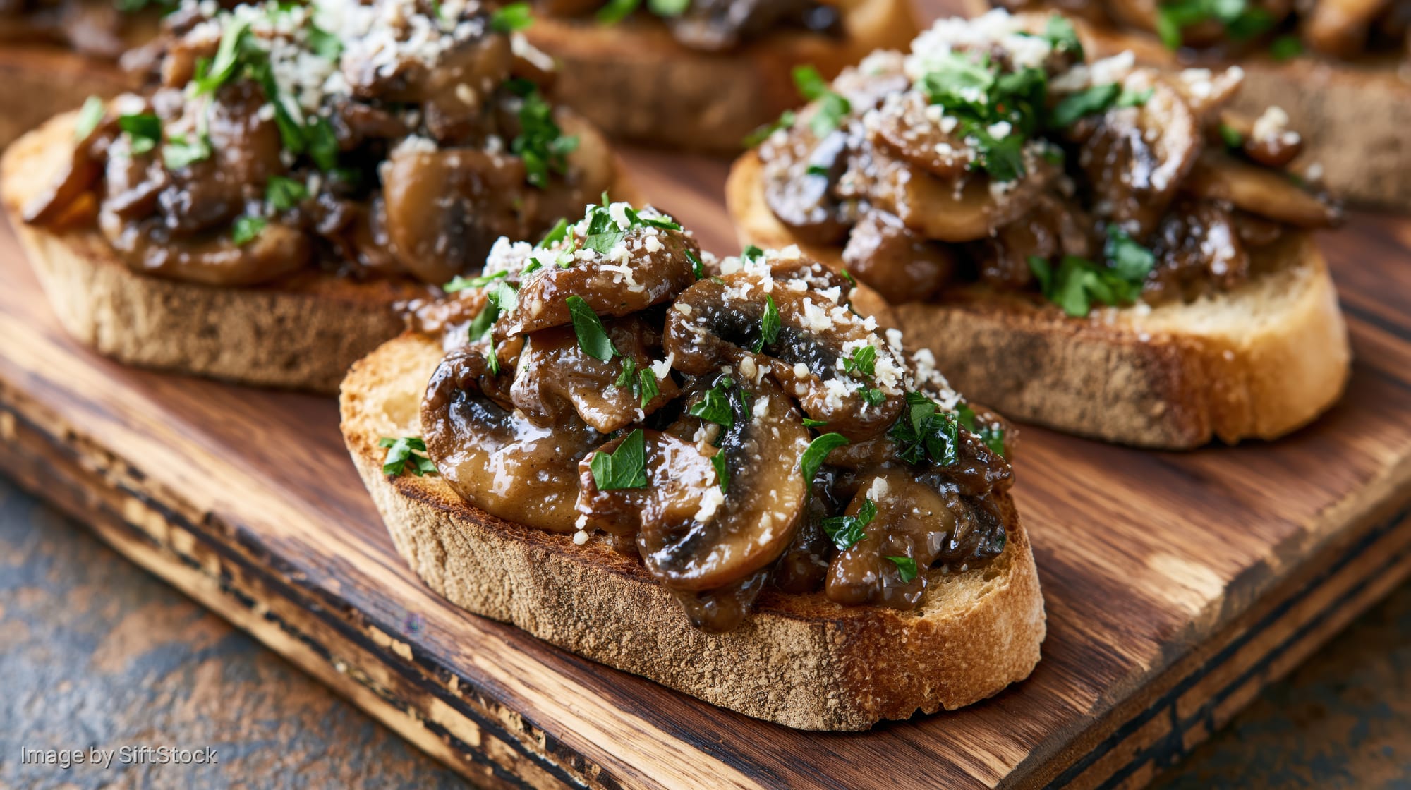 Mushroom bruschetta on toasted sourdough bread topped with parsley and cheese on a wooden board