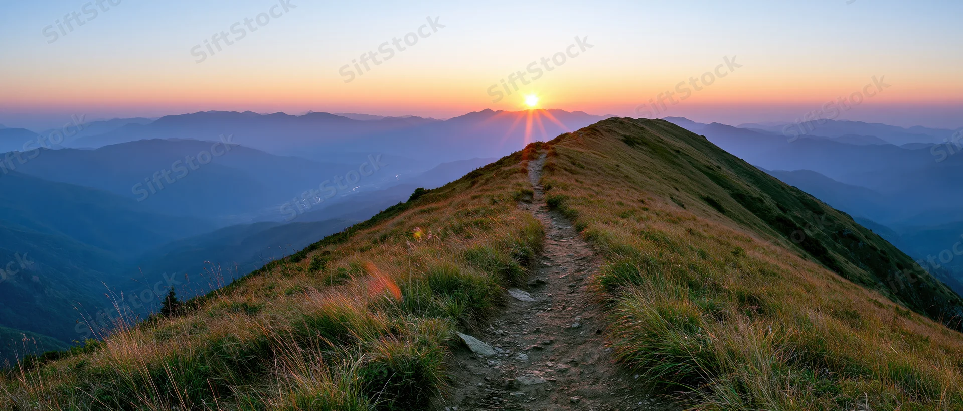Narrow dirt trail winding along mountain ridge toward setting sun at dusk