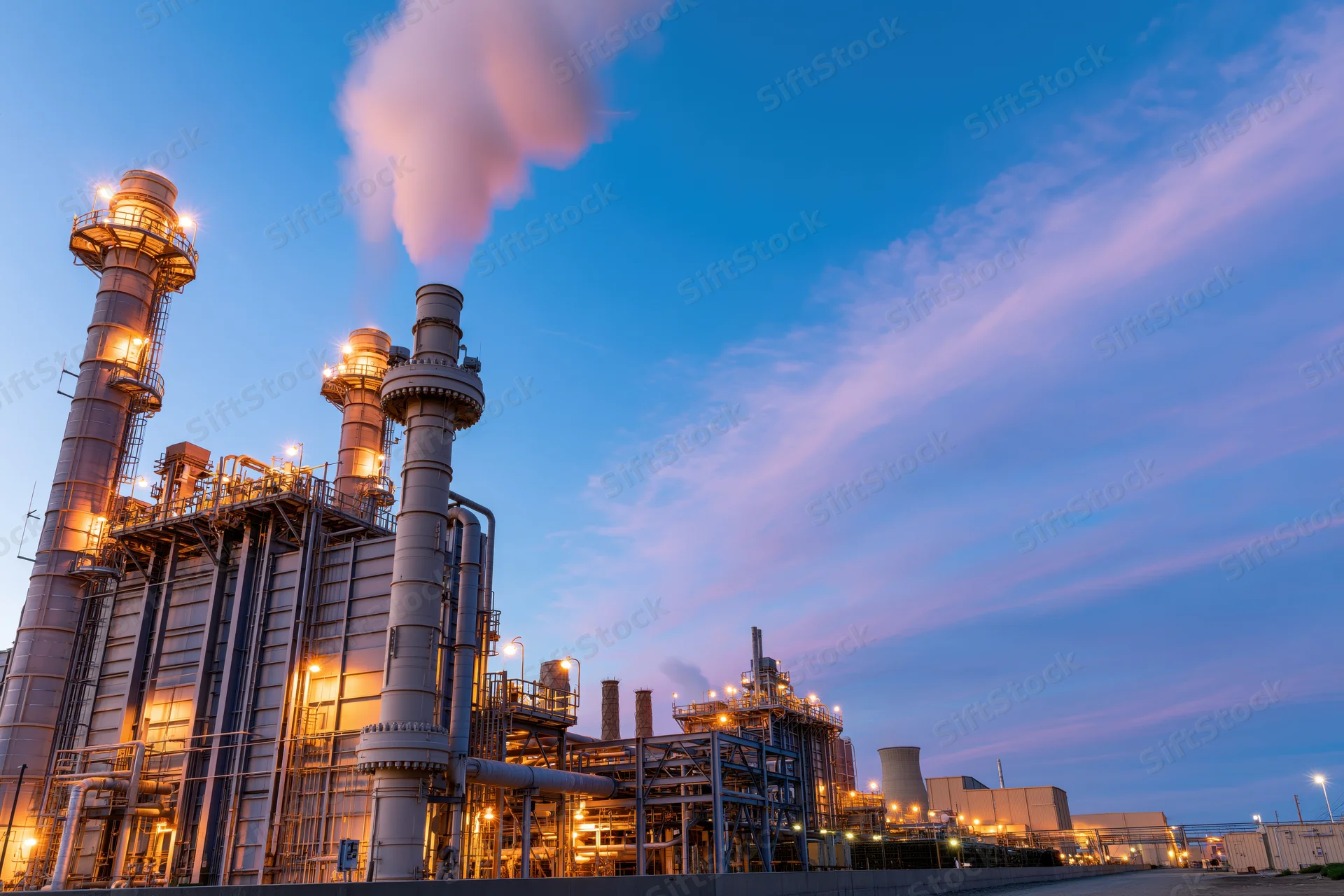 Natural gas power plant with illuminated towers and steam rising at twilight