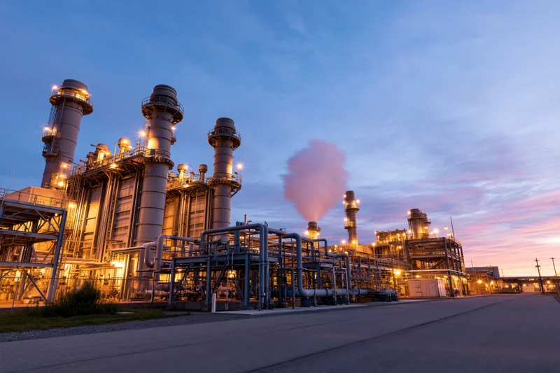 Natural gas power plant with illuminated towers and steam rising at twilight
