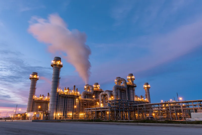 Natural gas power plant with illuminated towers and steam rising at twilight