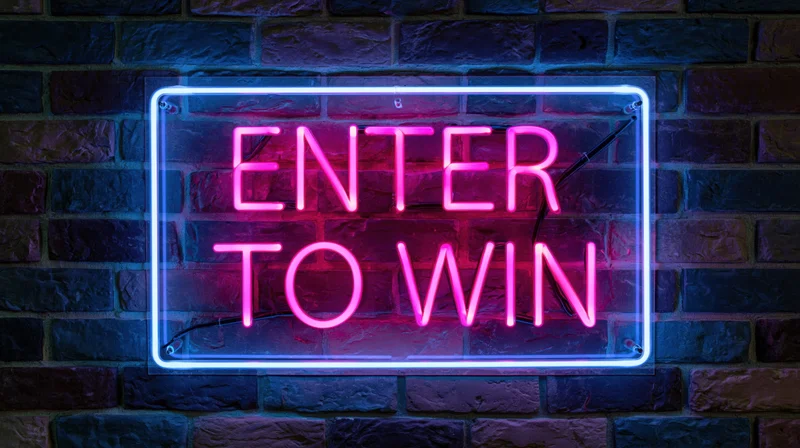 Neon sign reading enter to win in pink glowing letters on a brick wall