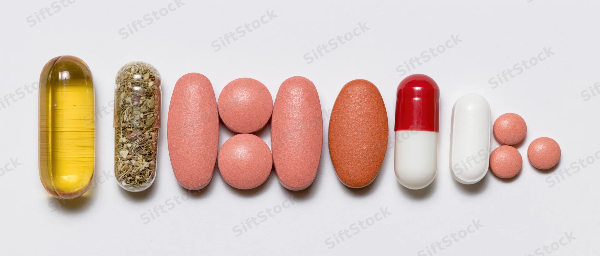 Assorted supplements and capsules arranged in a row on white background
