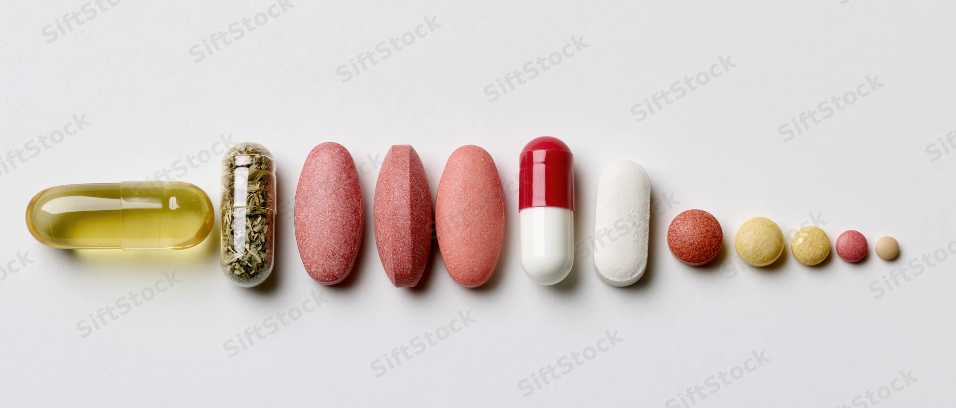 Assorted pills and capsules arranged in a horizontal row on white background