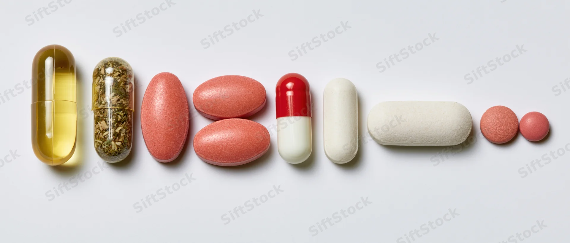 Assorted pills and capsules arranged in a horizontal row on a white surface