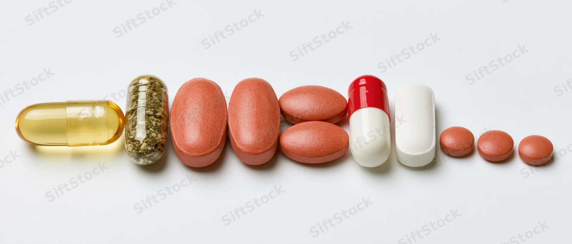 Assorted pills and capsules arranged in a horizontal row on white background