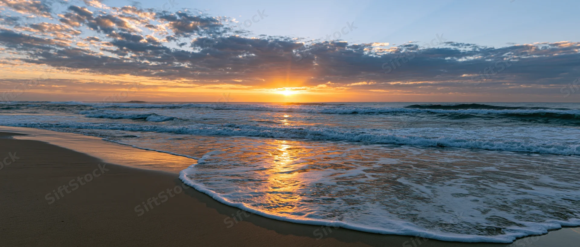 Ocean waves breaking on wet sandy beach at sunrise