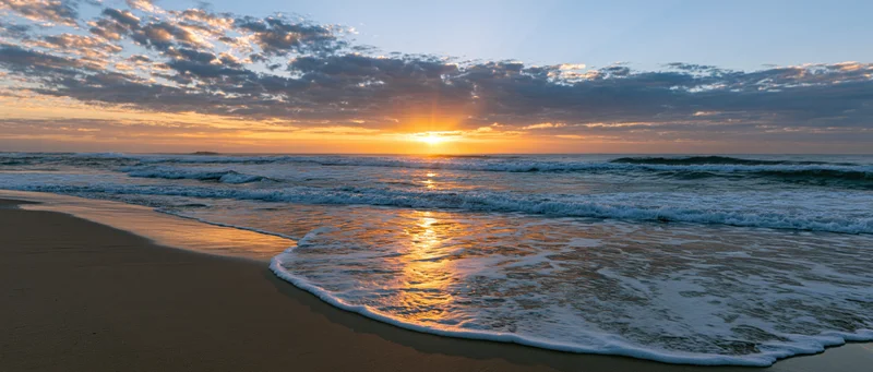 Ocean waves breaking on wet sandy beach at sunrise