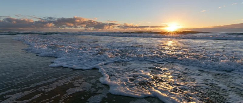 Ocean waves breaking on wet sandy beach at sunrise