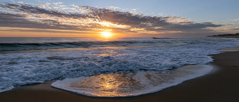Ocean waves breaking on wet sandy beach at sunrise