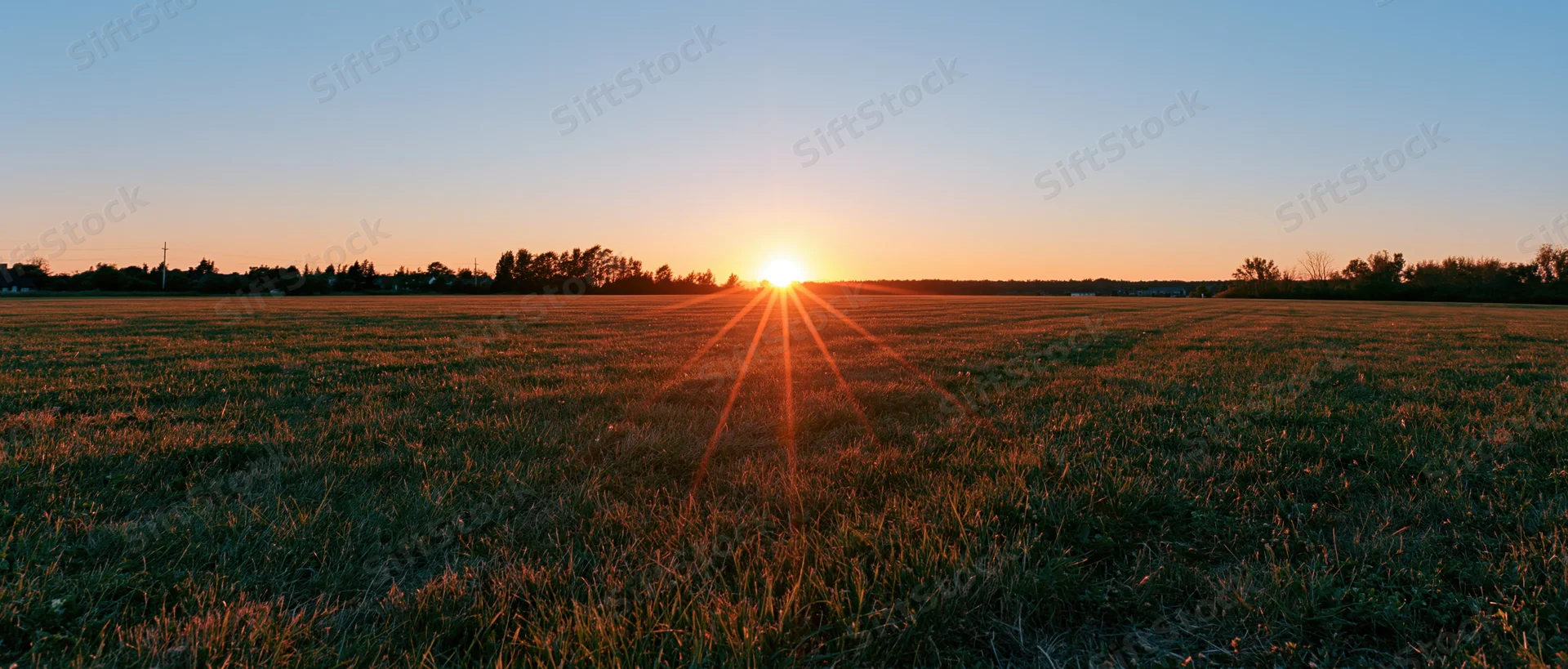 Sunset over an open grass field with sun just above the horizon