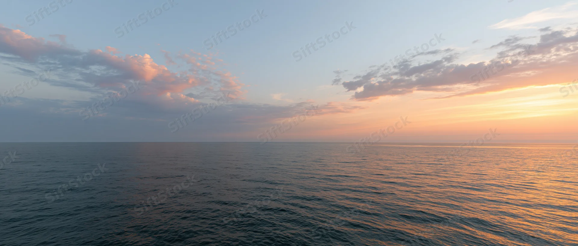 Open ocean at sunset with calm water reflecting warm orange sky