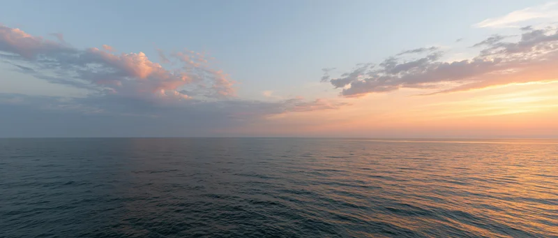 Open ocean at sunset with calm water reflecting warm orange sky