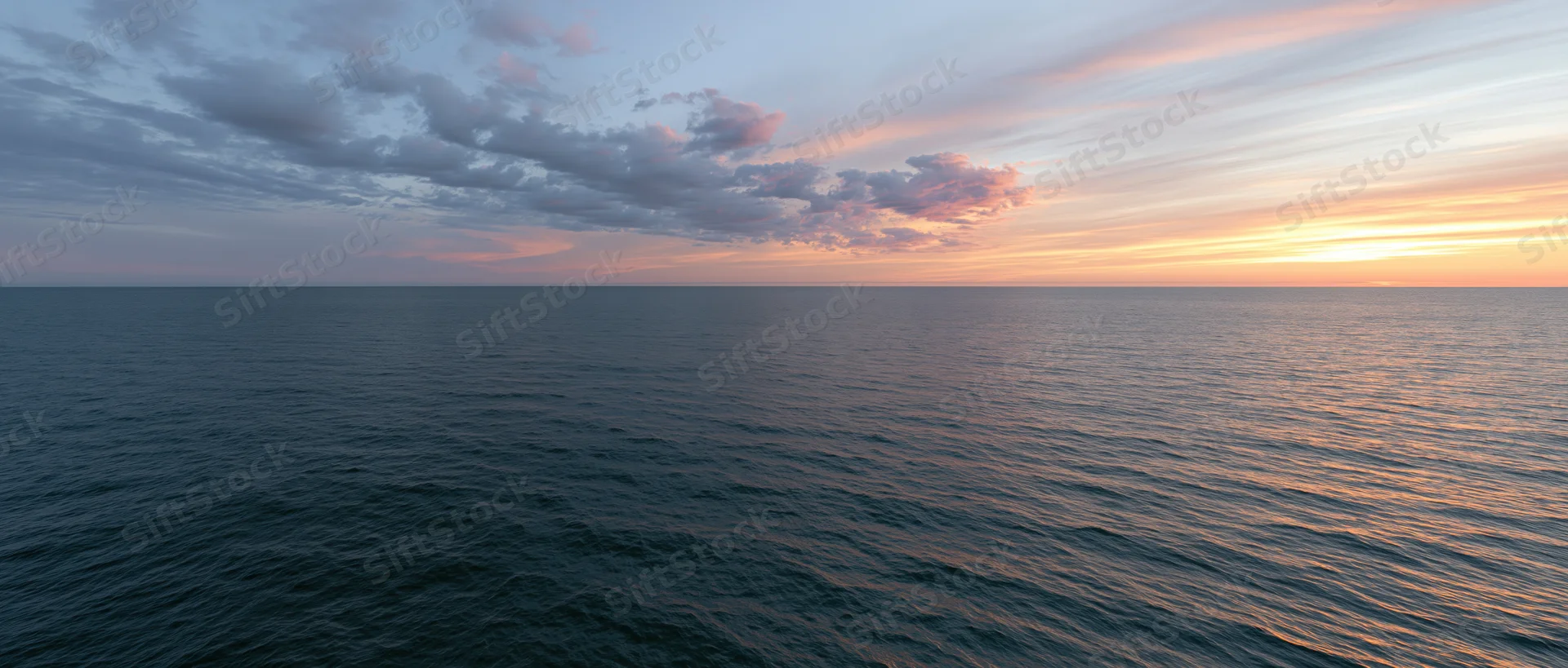 Open ocean at sunset with calm water reflecting warm orange sky and scattered clouds along the horizon