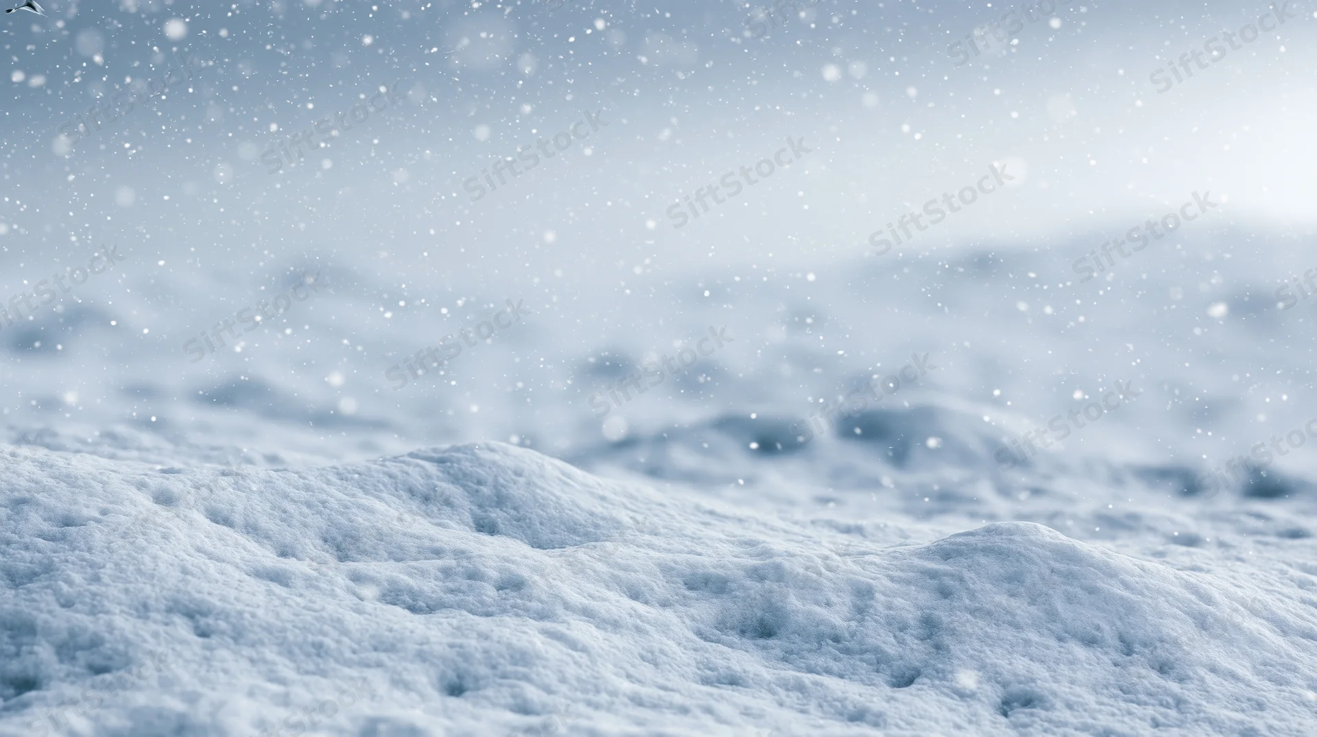 Snowy landscape during active snowfall with snowdrifts and falling snowflakes under overcast sky