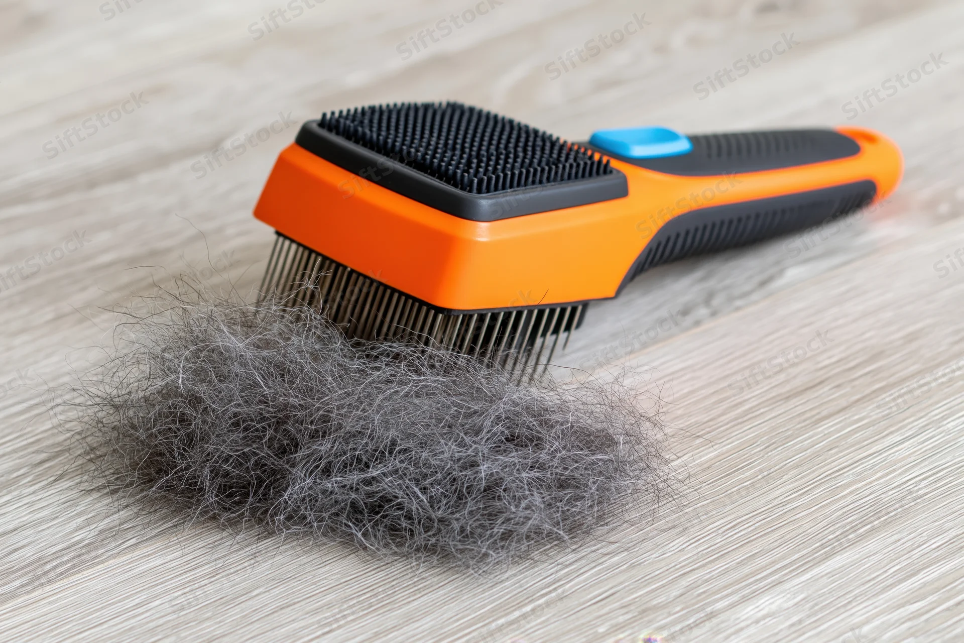 Orange and black pet deshedding brush with collected fur on wooden floor