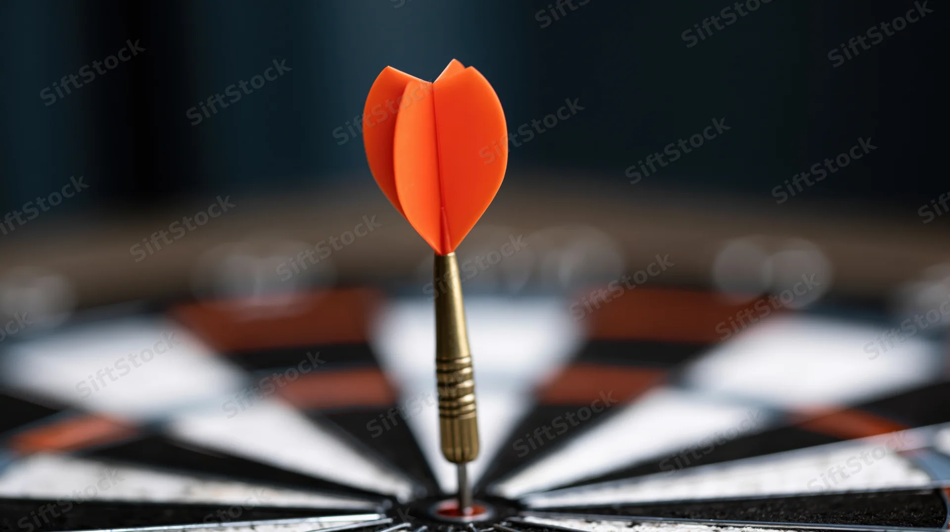 Orange dart with metallic barrel stuck dead-center in a black and white dartboard