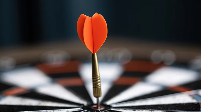 Orange dart with metallic barrel stuck dead-center in a black and white dartboard
