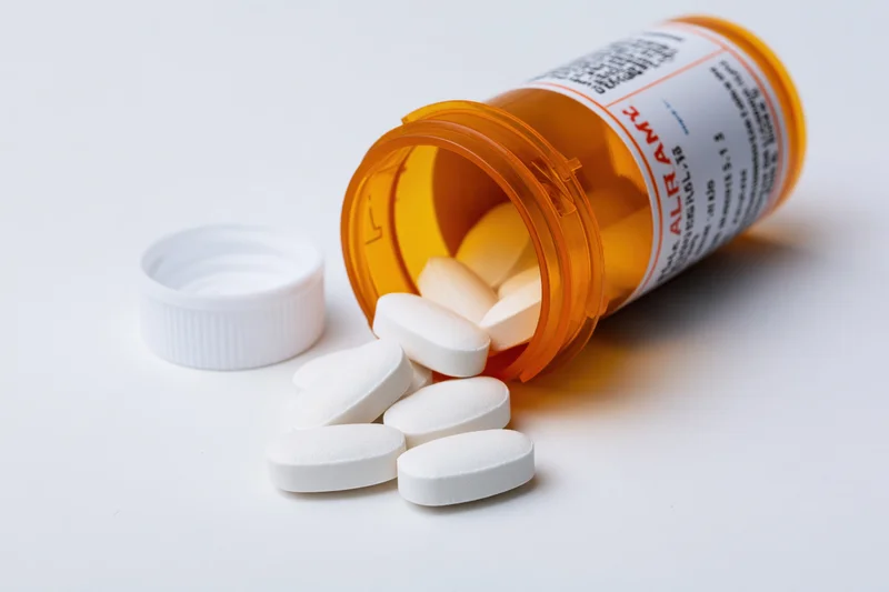 Orange prescription bottle lying on its side with white pills spilled out on white surface