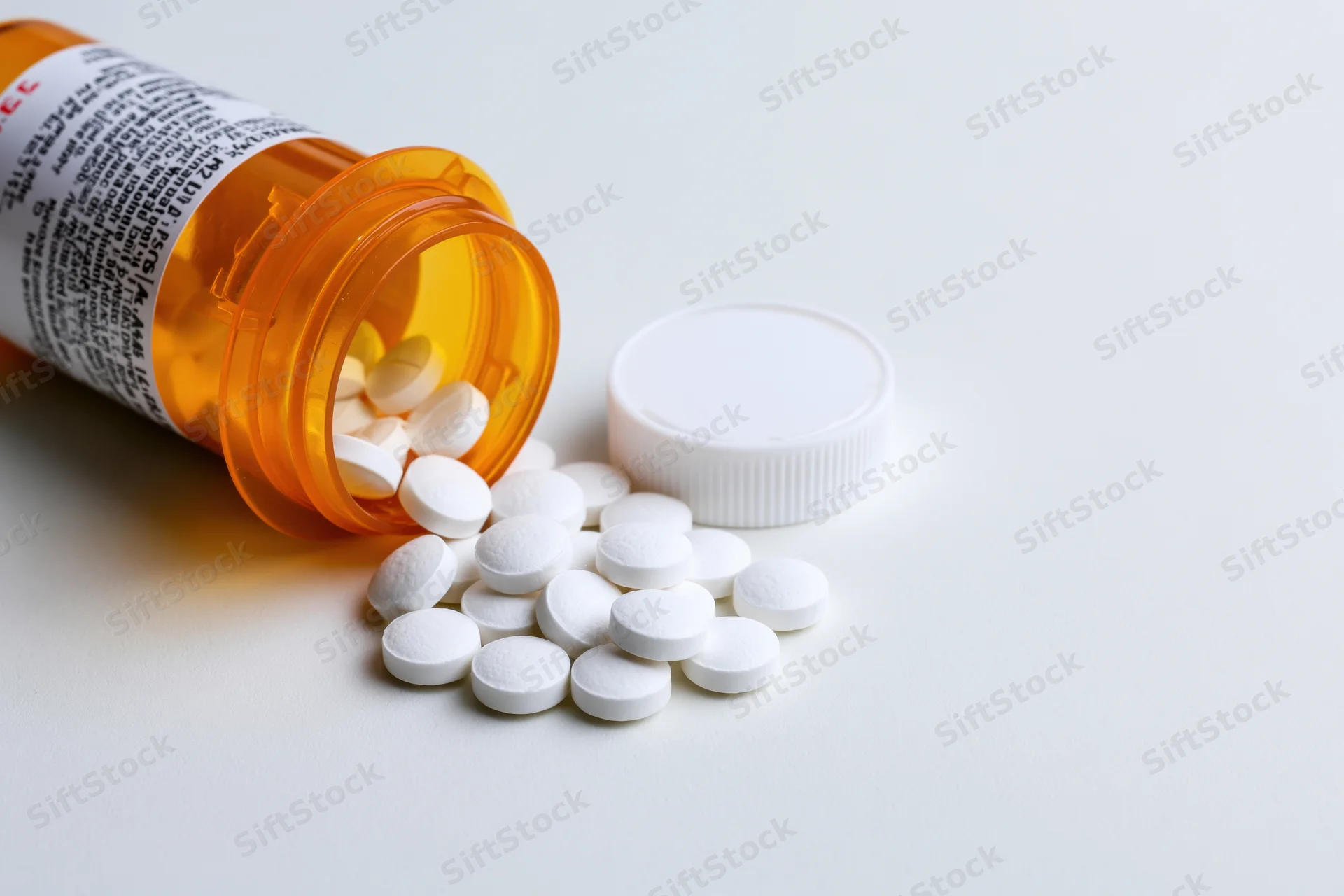 Orange prescription bottle tipped over with white pills spilled onto white surface