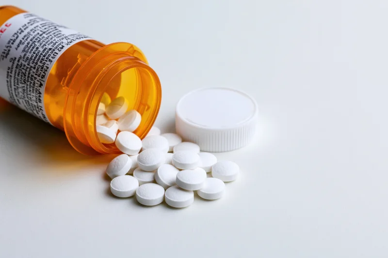 Orange prescription bottle tipped over with white pills spilled onto white surface