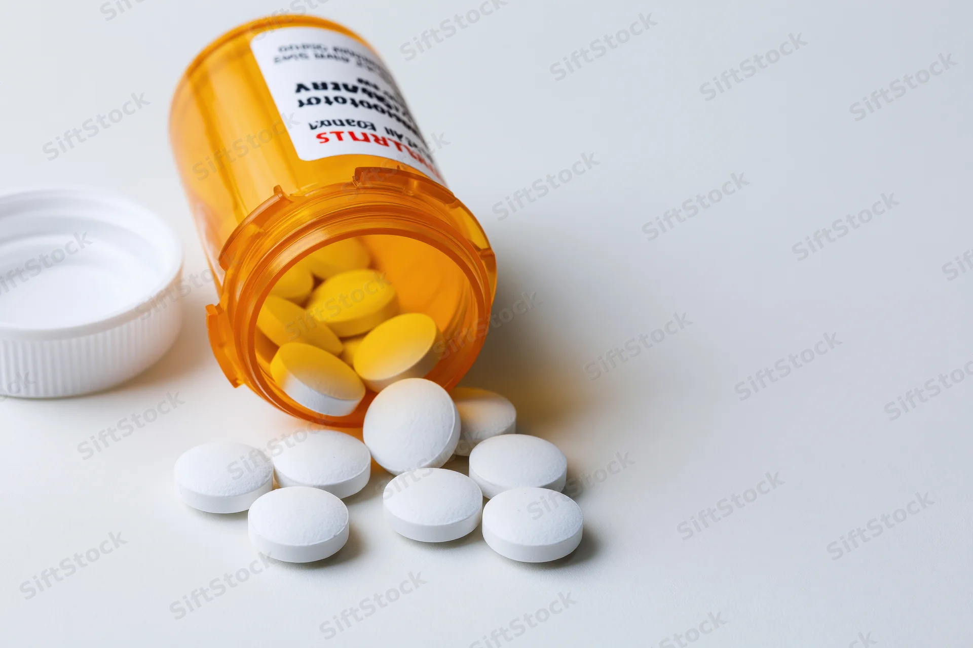 Orange prescription bottle lying on its side with white pills spilled onto a white surface