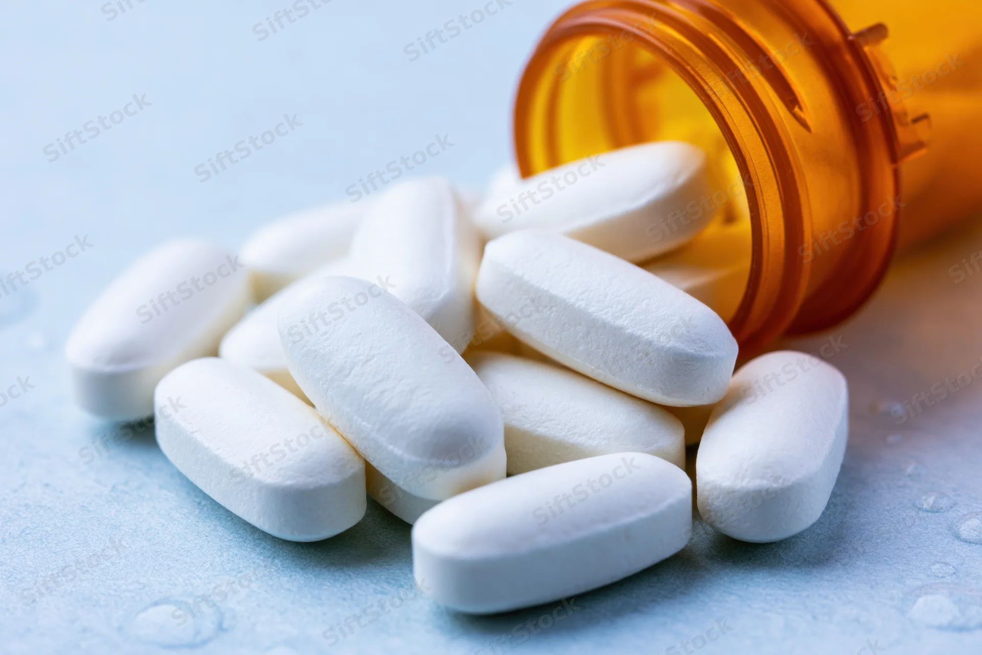 White pills spilled from an orange prescription bottle on a light blue surface