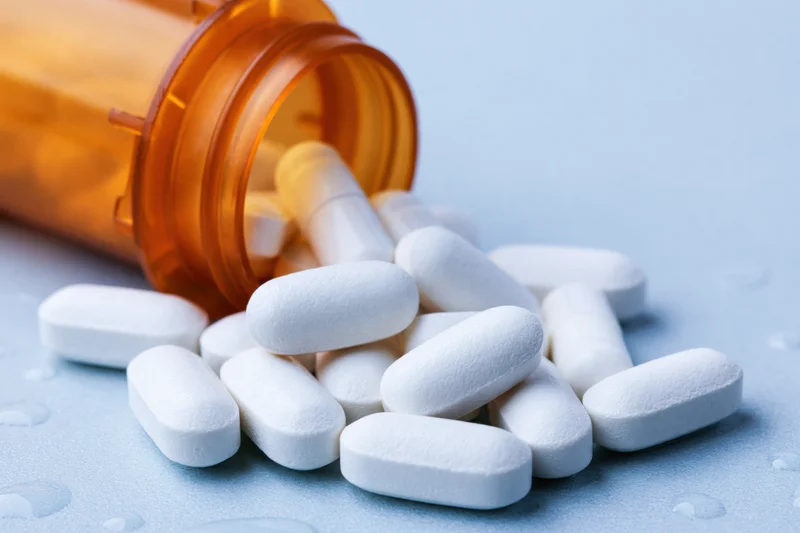 White oval pills spilling from an orange prescription bottle onto a light blue surface
