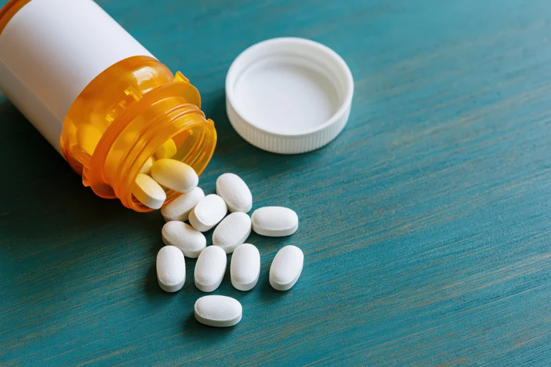 Orange prescription bottle tipped over with white pills spilled onto teal wooden surface