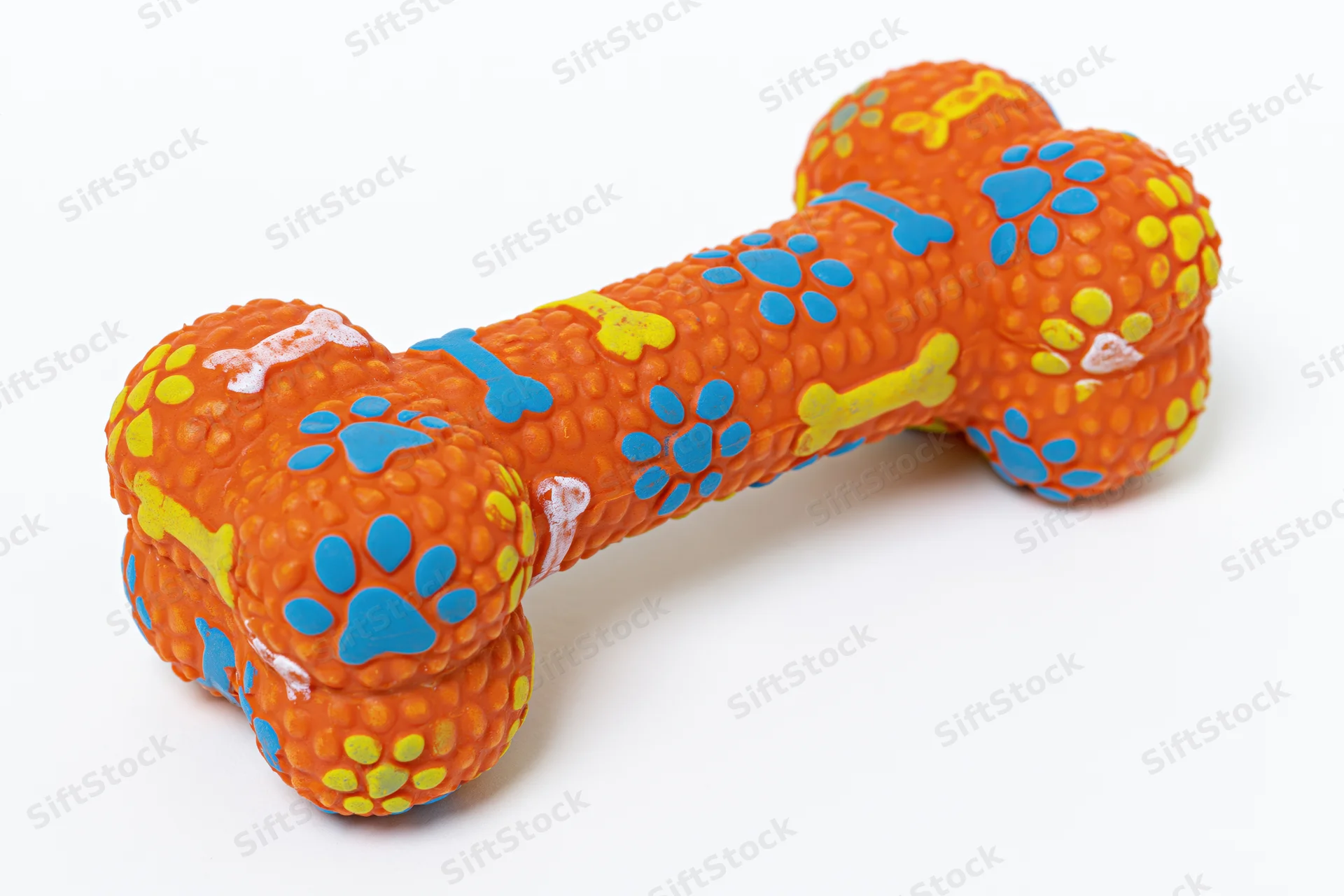 Orange rubber dog chew toy shaped like a bone with blue and yellow paw prints and bone patterns on white background