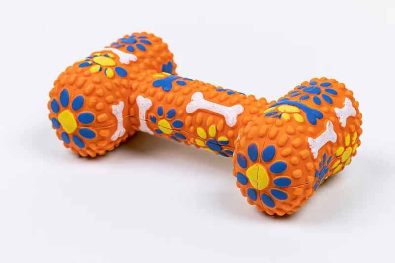 Orange rubber dog chew toy shaped like a dumbbell bone with blue and yellow patterns on white background