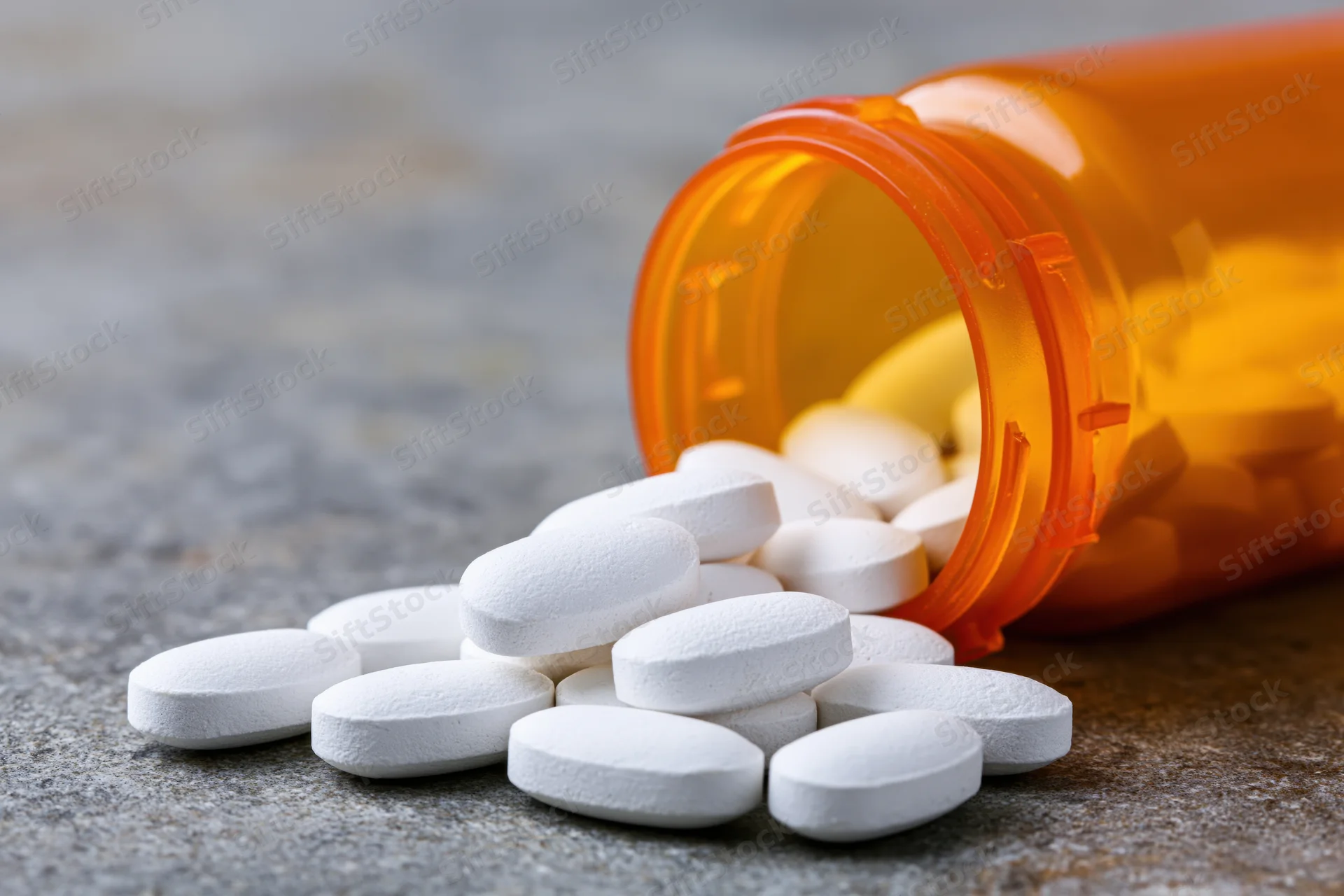 White oval pills spilled from an orange prescription bottle on a textured surface