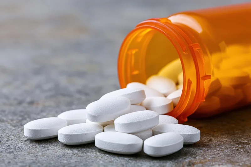 White oval pills spilled from an orange prescription bottle on a textured surface