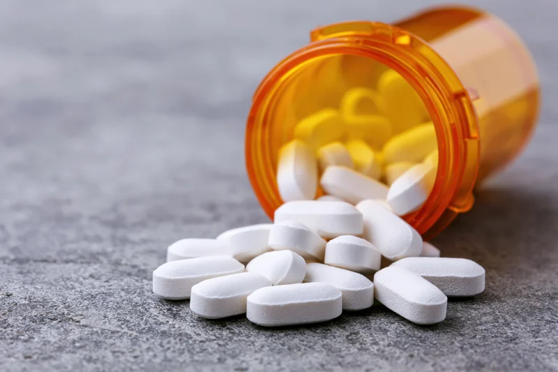 White oval pills spilled from an orange translucent prescription bottle on a gray surface