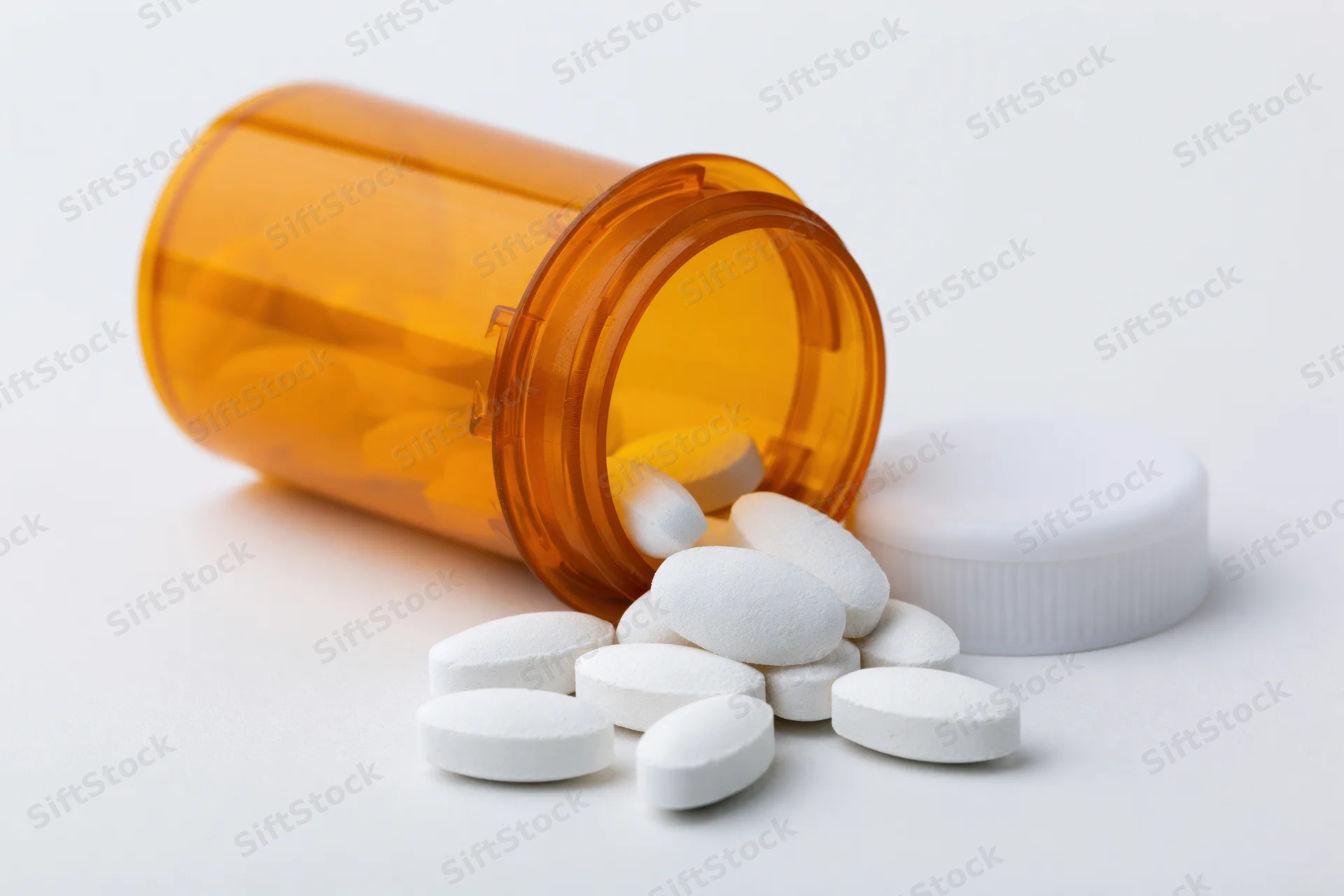 Orange prescription bottle tipped over with white pills spilling out on white surface