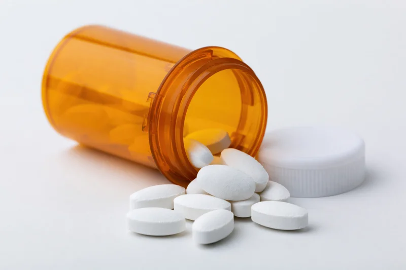 Orange prescription bottle tipped over with white pills spilling out on white surface