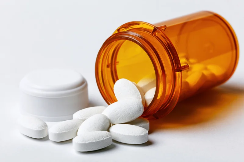 White pills spilling from an amber prescription bottle on a white surface