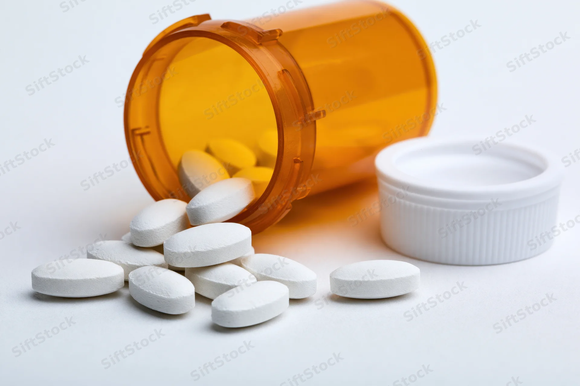 Orange prescription bottle tipped over with white pills spilled onto white surface
