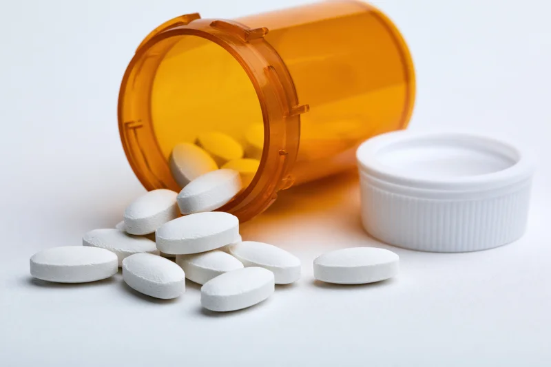 Orange prescription bottle tipped over with white pills spilled onto white surface