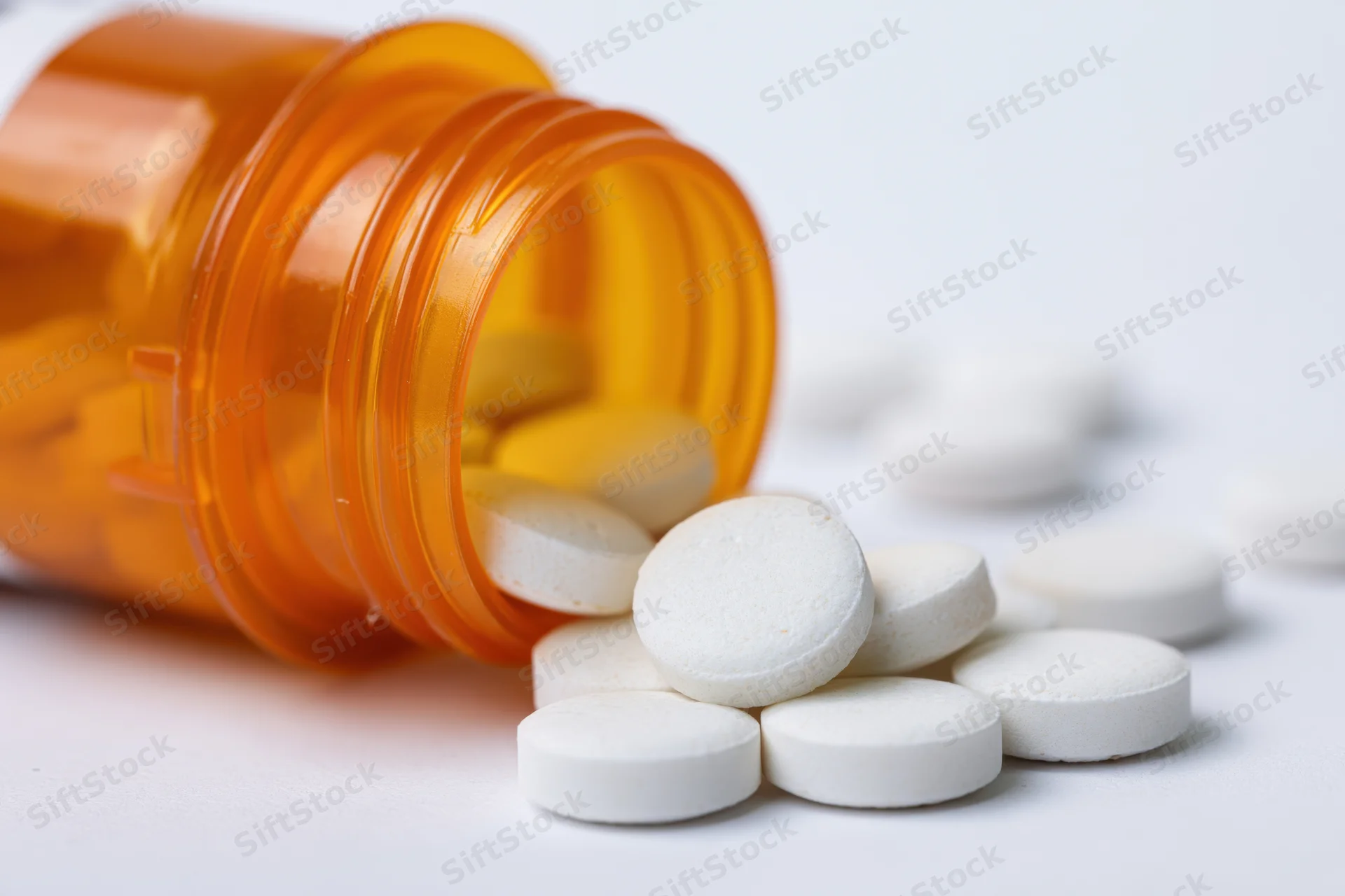 Orange prescription bottle tipped over with white pills spilling onto white surface