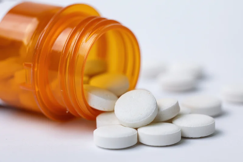 Orange prescription bottle tipped over with white pills spilling onto white surface