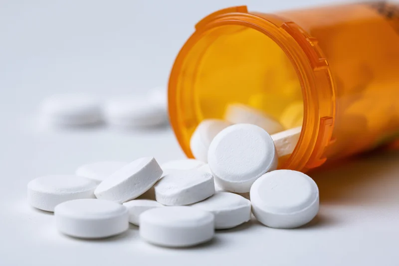 White tablets spilled from an orange prescription bottle on a white surface