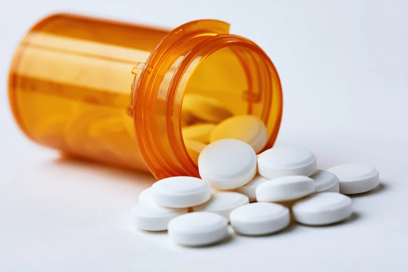 Orange prescription bottle tipped over with white tablets spilled onto white surface
