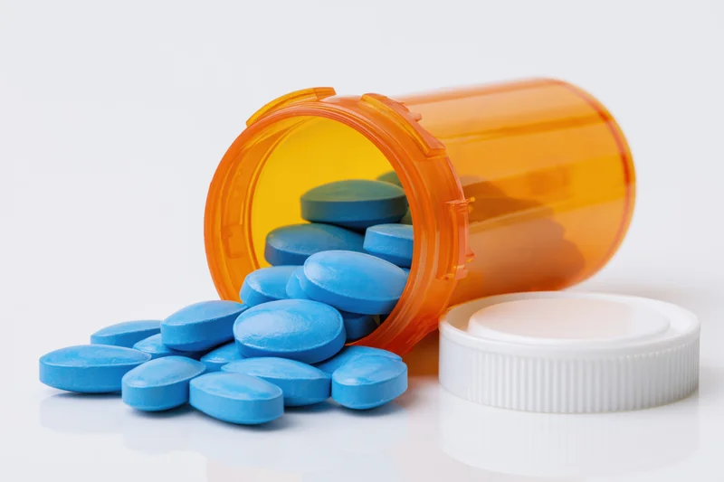 Blue pills spilling from an orange prescription bottle on a white surface
